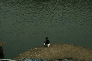 10 Ways to Cultivate Resilience in Difficult Times 3 a person sitting on a rock near water, Difficult Times